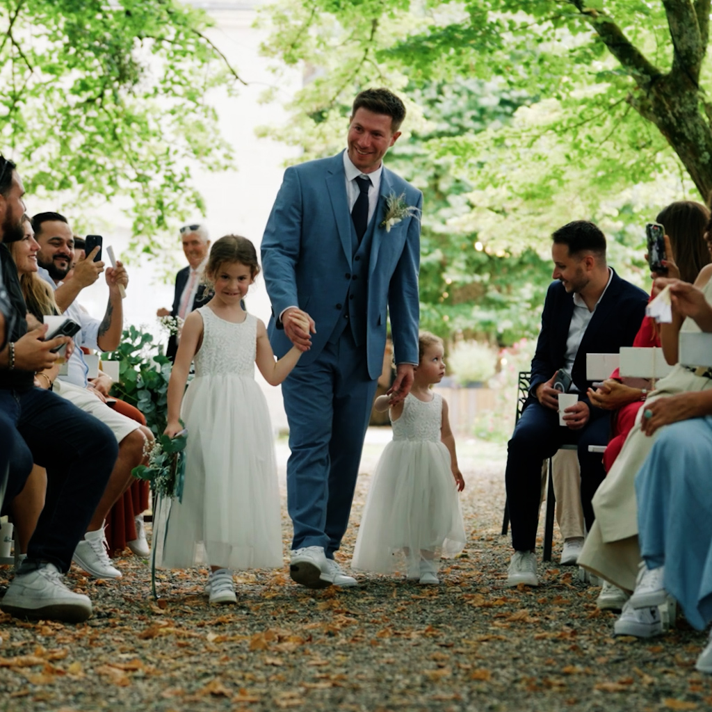 Un film de mariage en Gironde Le marié descend l'allée avec ses deux filles et tout le monde les regarde - film de mariage basé à Toulouse