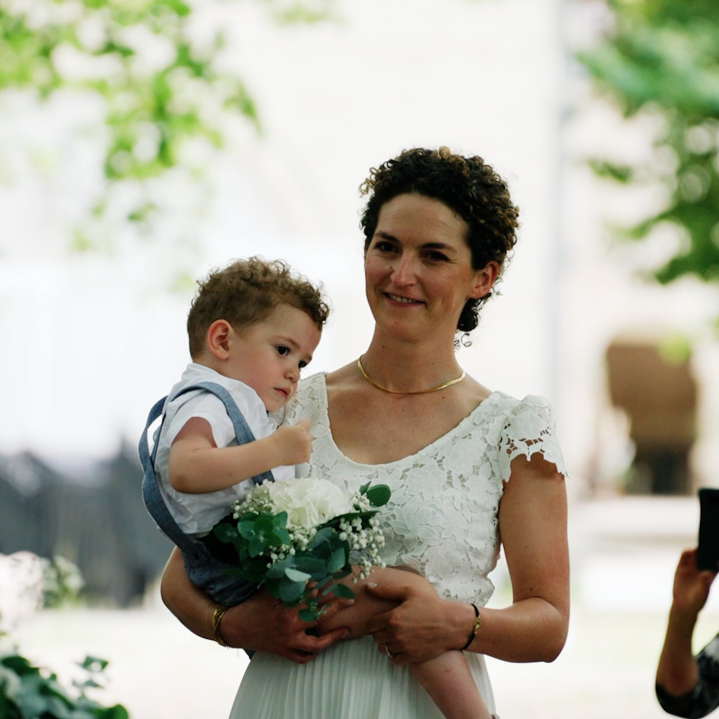 La mariée, belle dans sa robe, avance dans l'allée avec son fils dans ses bras - extrait de son film de mariage réalisé à Toulouse